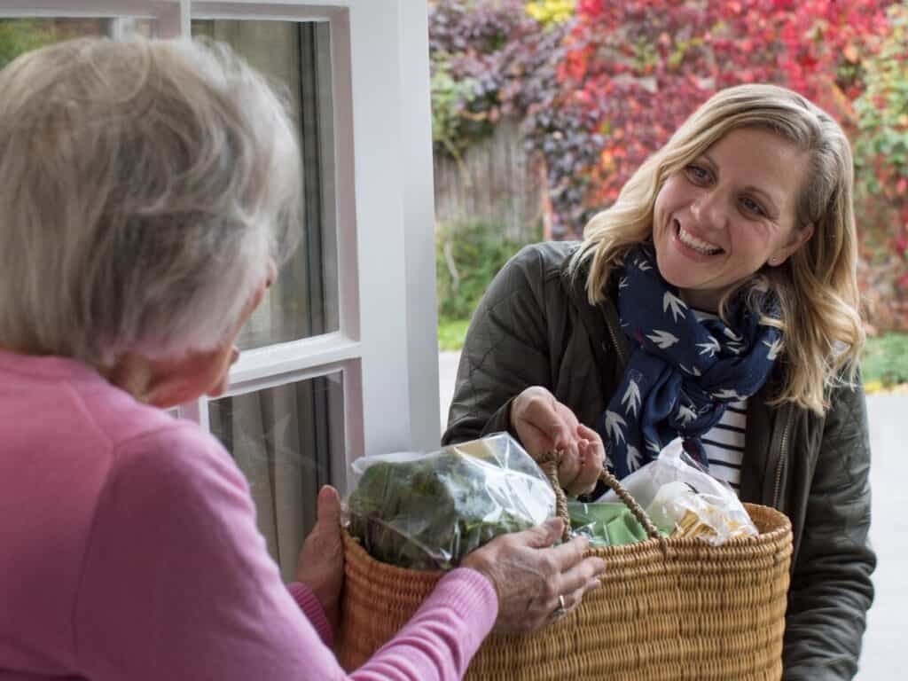 a woman handing a bag of groceries to an old woman